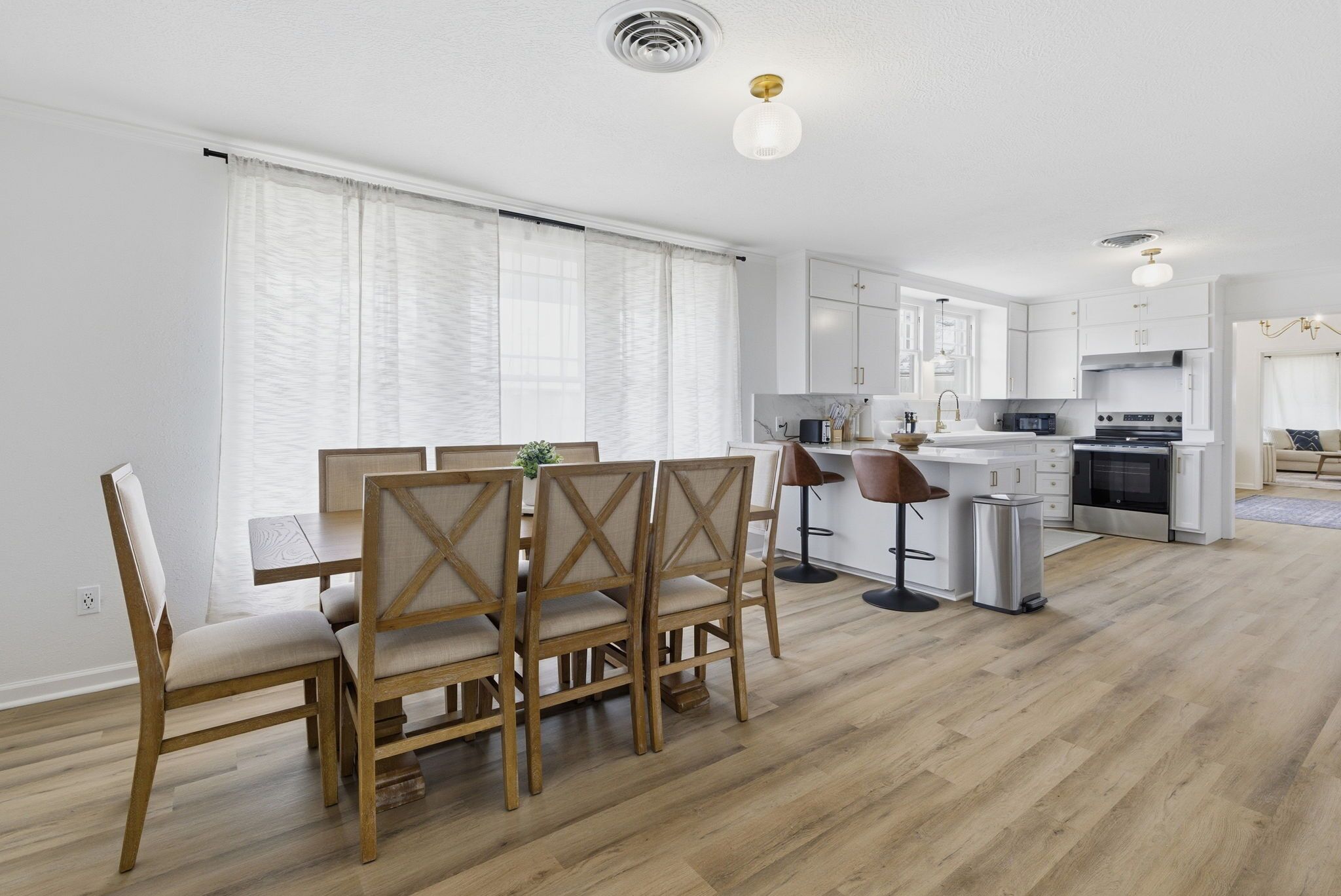 A modern kitchen with white cabinets, a dining area with wooden chairs, and a bar stool.