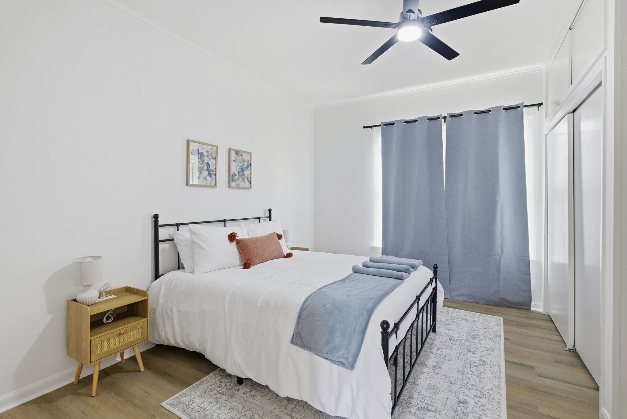 A bedroom with a bed, a nightstand, a ceiling fan, and a window with curtains.