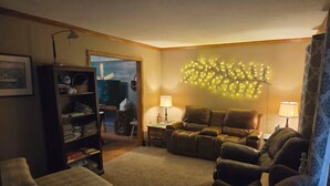Una sala de estar acogedora con chimenea, sofás de cuero, una estantería y un elemento decorativo de luz en la pared.