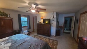 Un dormitorio con cama, ventilador de techo, cómoda, televisor y ventana.