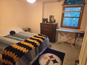 A bedroom with a bed, a dresser, a desk, and a window with blinds.