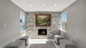 A modern living room with a stone fireplace, a framed painting above it, and two grey sofas.
