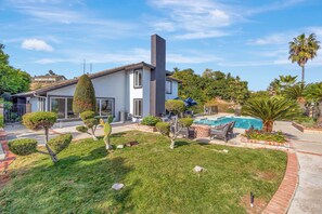 A modern house with a swimming pool, well-maintained lawn, and various plants.