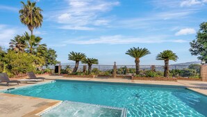 A swimming pool with clear water, surrounded by palm trees and a fence.