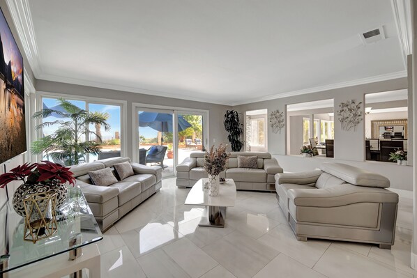 A spacious living room with a large window, a glass coffee table, and a beige sofa.
