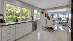 A modern kitchen with white cabinets, a dishwasher, and a dining area with white chairs and a table.