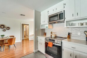A modern kitchen with white cabinets, a microwave, an oven, and a dining area with a wooden table and chairs. - Private Pool & Yard: Tempe Family Gem Near ASU! (Tempe)