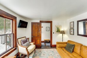 Una sala de estar acogedora con un piso de madera, un sofá, un sillón y un televisor montado en la pared.