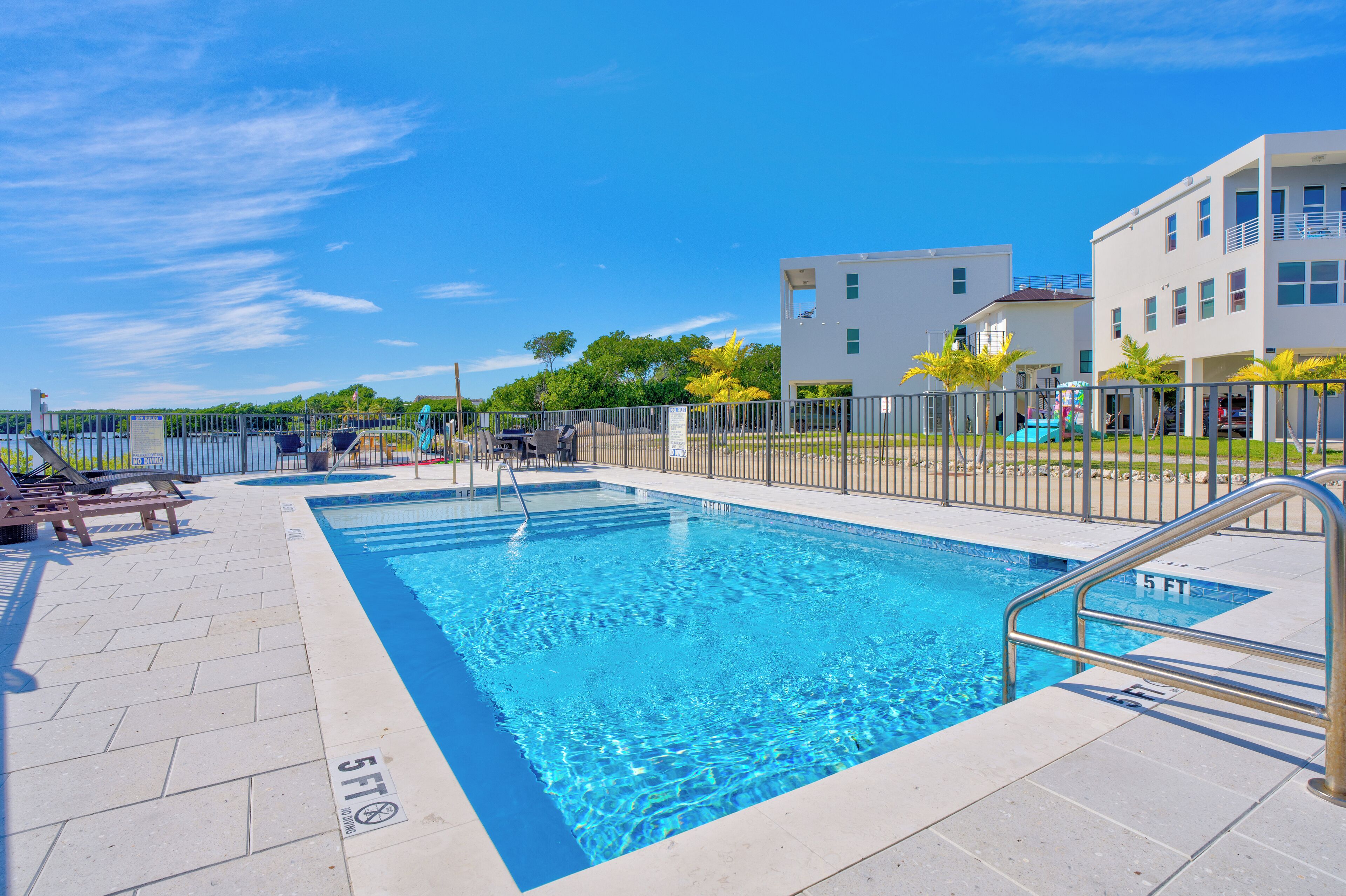 Una piscina con una marca de profundidad de 1.5 metros, rodeada de una valla y sillas de descanso.