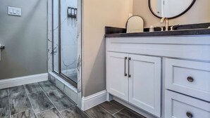 A bathroom with a glass shower enclosure, a vanity with a mirror, and a tiled floor.