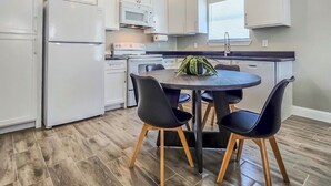 A modern kitchen with white cabinets, a black countertop, and a dining table with four chairs.