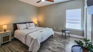 A bedroom with a bed, nightstands, a ceiling fan, a window with blinds, and a small table with a plant.