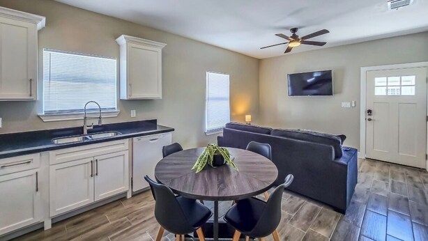 A modern kitchen with white cabinets, a dark countertop, and a dining area with a round table and chairs.