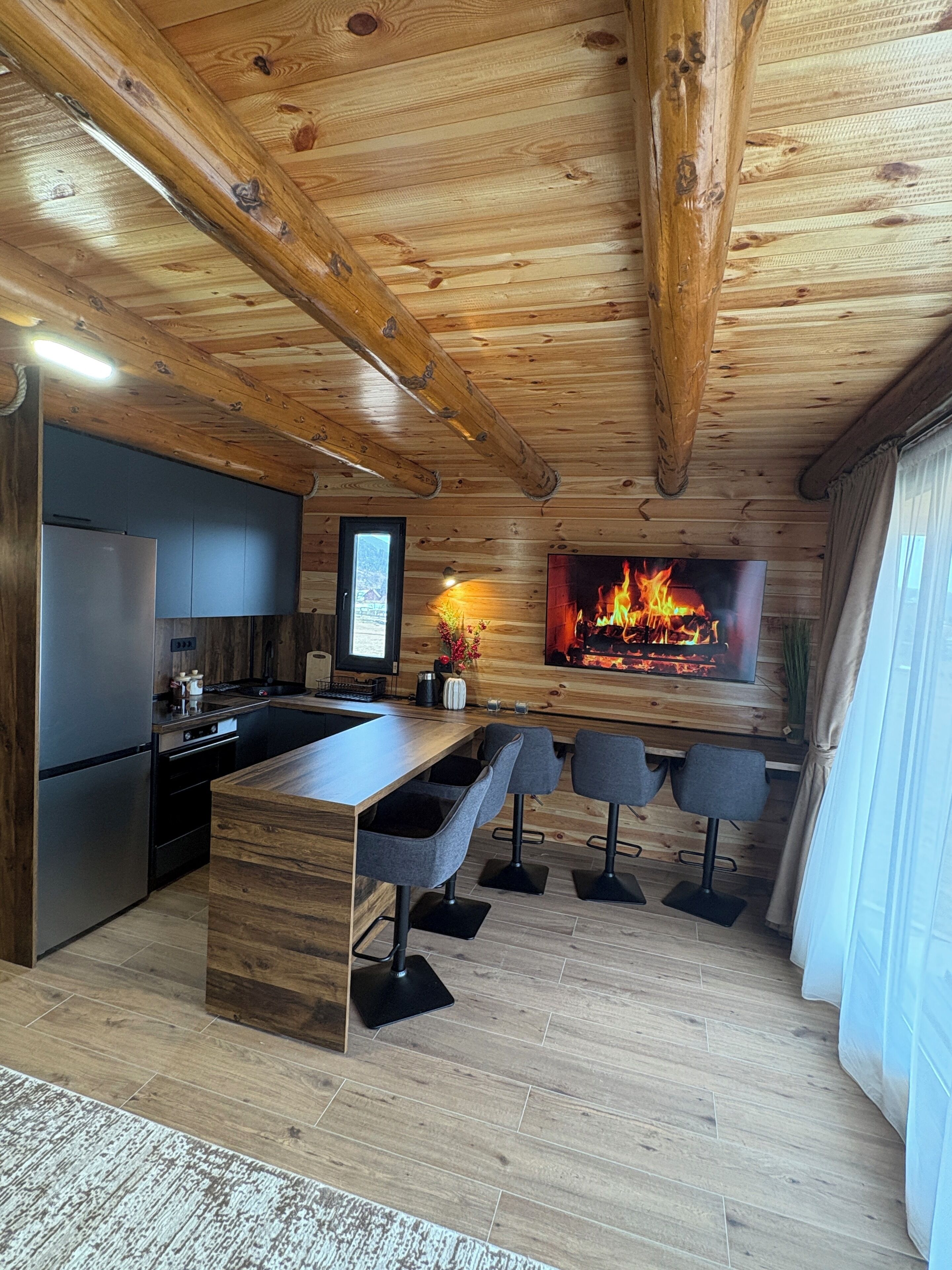 A modern kitchen with a built-in refrigerator and stove, a wooden island with bar stools, and a fireplace with a TV above it.