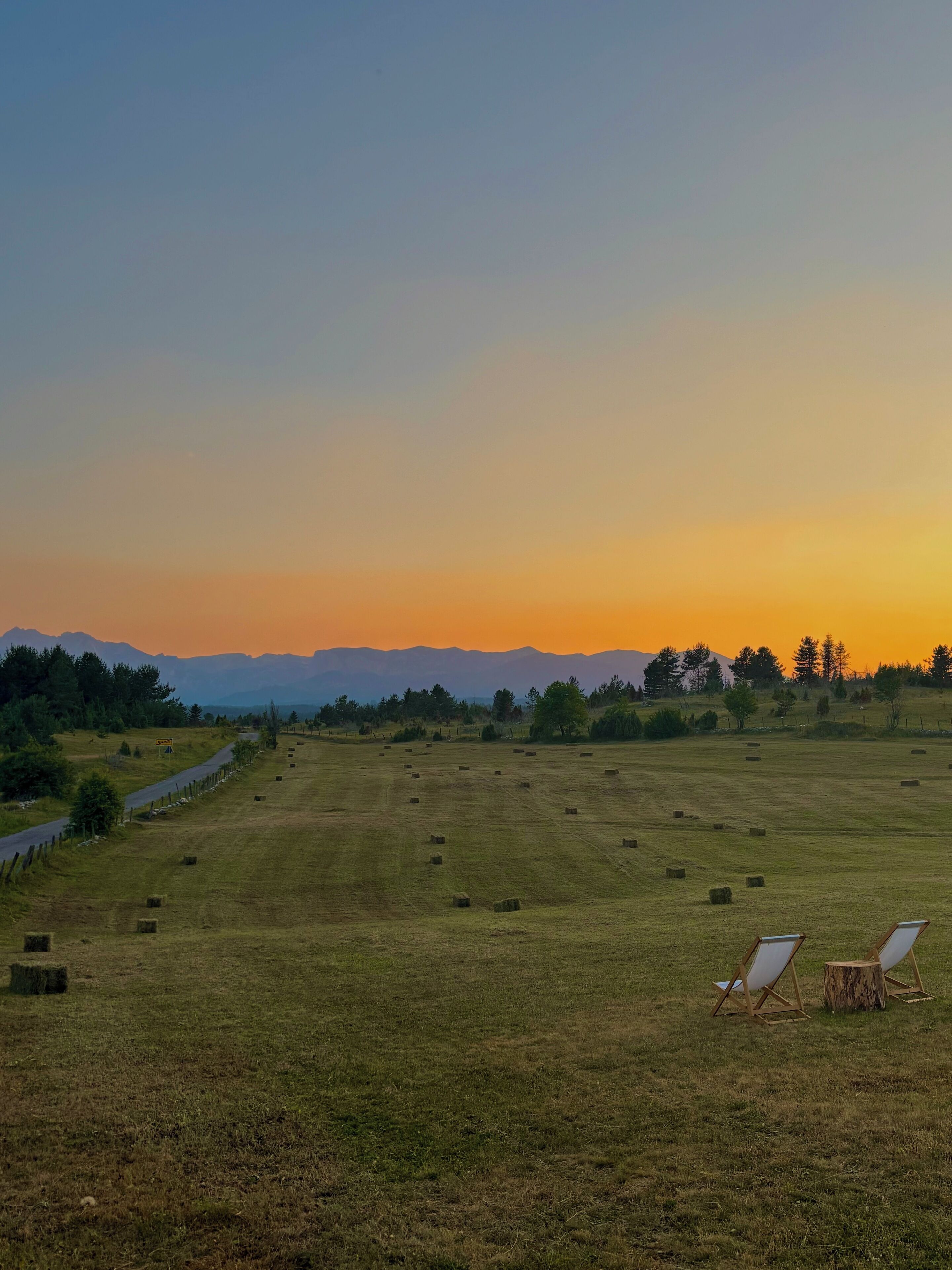 Een grasveld met hooibalen en twee houten stoelen.