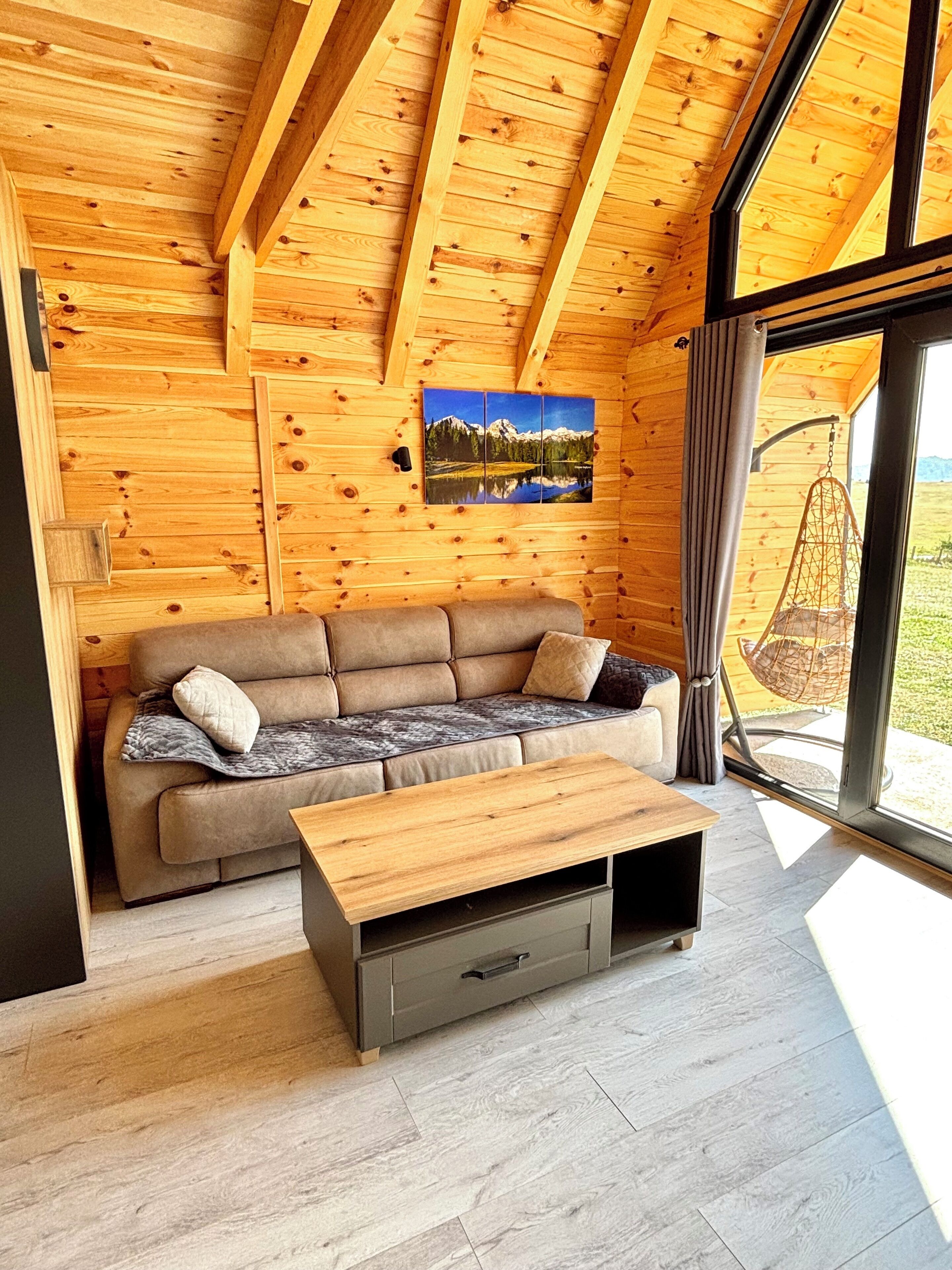 Une pièce chaleureuse avec un plafond en bois, un canapé, une table basse et une grande fenêtre donnant sur l’extérieur.