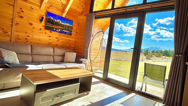 L'interno di una baita in legno con un'ampia finestra, un divano e un tavolino in legno.