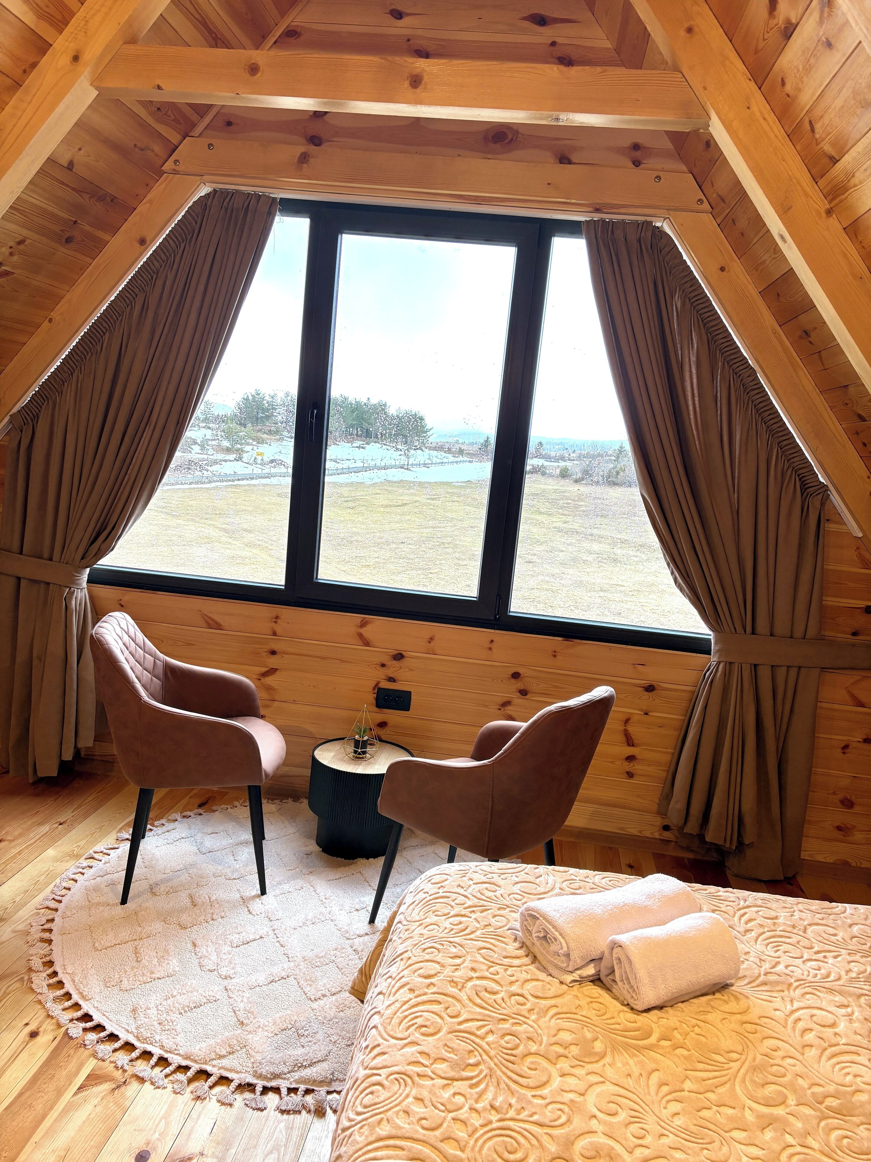 Una habitación acogedora con una cama, dos sillas, una mesita y una ventana con cortinas.