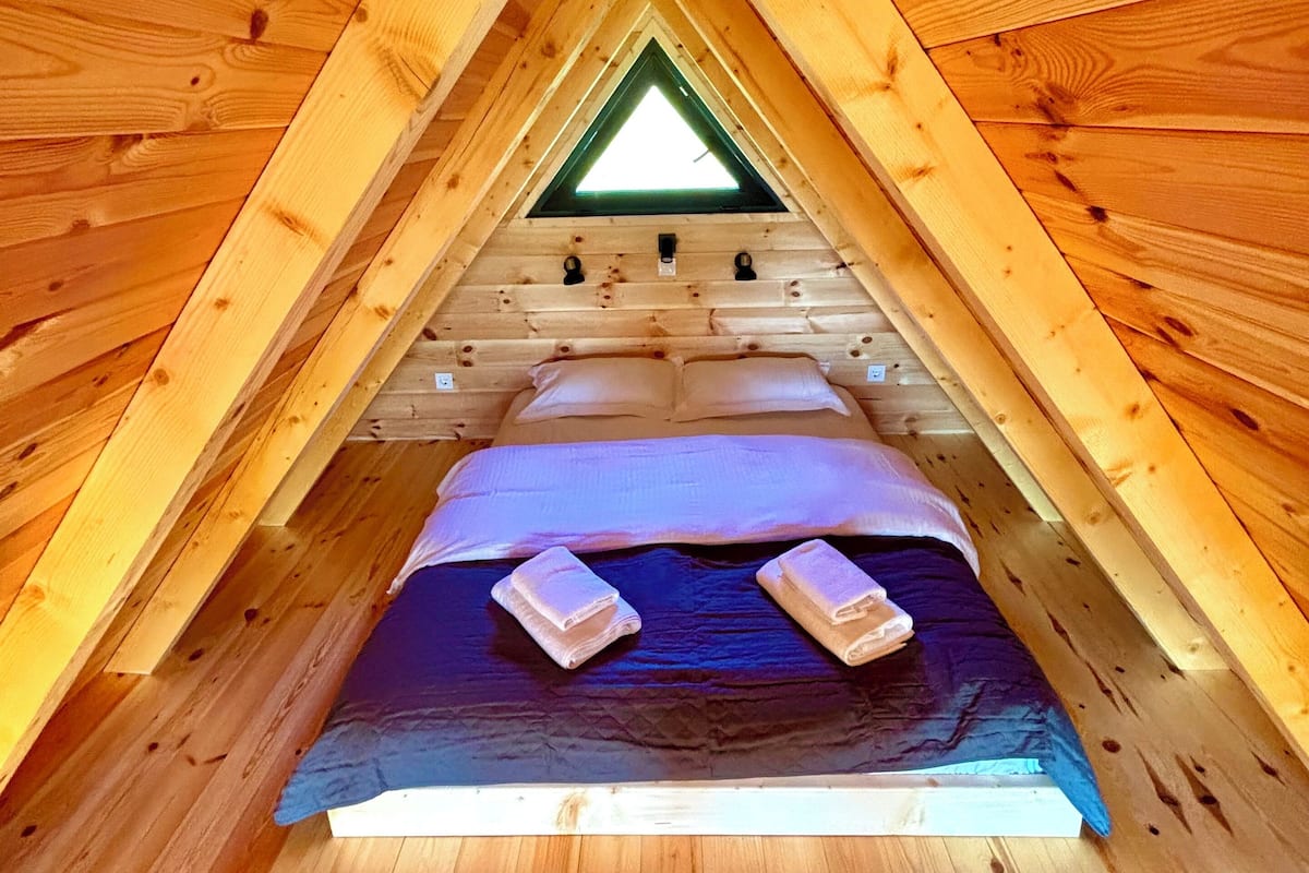 A small, triangular wooden room with a bed, pillows, and towels.