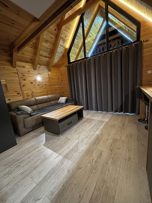 A cozy attic bedroom with a wooden ceiling, a sofa, a small table, and a window with curtains. - Eternum Glampling (Ninkovići)
