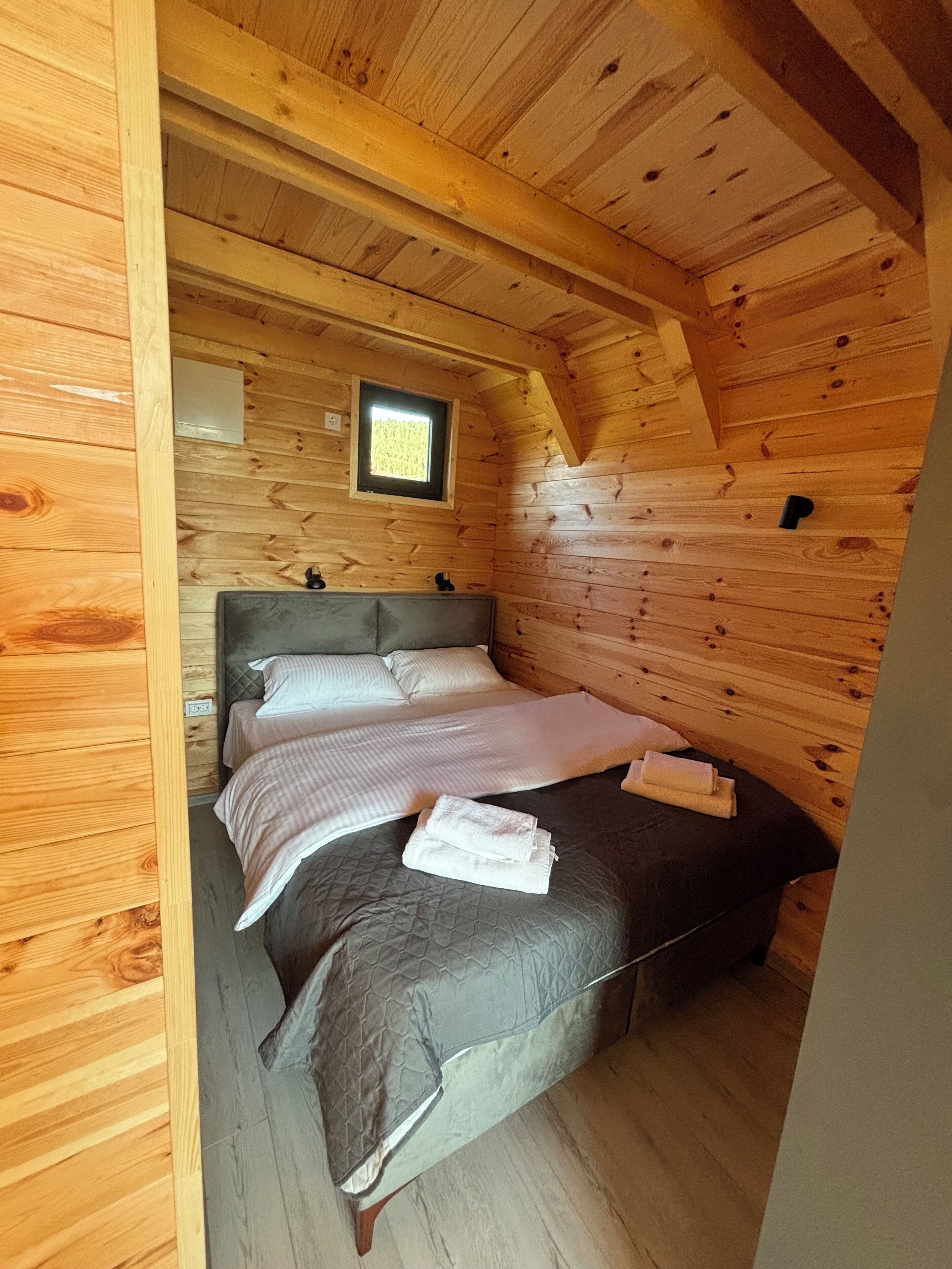 Une chambre dans une cabane en bois, avec un lit, des oreillers et une petite fenêtre.