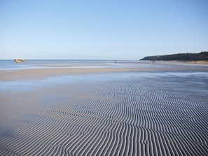 A beach with rippled sand patterns, a distant shoreline, and a few people in the background. - Lovely holiday home with direct sea view (Glesborg)