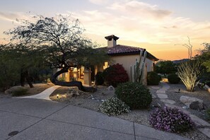 Une maison avec un chemin de pierre menant à l’entrée, entourée de différentes plantes et de cactus.
