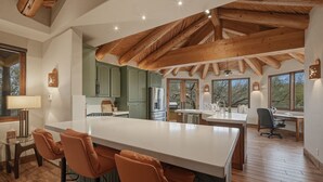 Una cocina amplia con una isla grande, vigas de madera, armarios verdes y una zona de comedor con taburetes de bar.