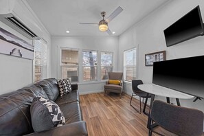 A modern living room with a leather sofa, a small round table, and a TV mounted on the wall.