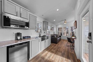 A modern kitchen with white cabinets, a built-in microwave, and a coffee station.