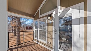 Eine überdachte Veranda mit Holzdeck, Metallgeländer und einer Glastür mit Fenster.