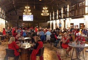 A spacious indoor dining area with high ceilings, chandeliers, and a large screen displaying a map. - The Resort at Fredericksburg Unit 24 (Fredericksburg)