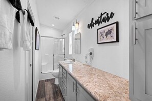 A modern bathroom with a marble countertop, a sink, a toilet, and a shower. There is a towel rack with towels, a framed world map, and a wall-mounted light fixture. - The Resort at Fredericksburg Unit 24 (Fredericksburg)