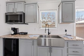 A modern kitchen with grey cabinets, a stainless steel sink, a coffee maker, and a window with blinds. - The Resort at Fredericksburg Unit 24 (Fredericksburg)