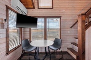 Ein gemütliches Cabin-Zimmer mit rundem Tisch und zwei Stühlen, Holzwänden, einem Wand-Fernseher und einer Treppe.