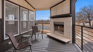 A covered deck with a stone fireplace, two wicker chairs, and large windows overlooking a landscape. - The Resort at Fredericksburg Unit 13 (Fredericksburg)
