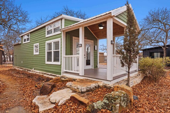 Una casa verde con portico e un piccolo giardino anteriore con rocce e un albero.