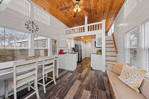 Une cuisine spacieuse avec des meubles blancs, un plafond en bois et un coin repas comprenant une banquette et des chaises.