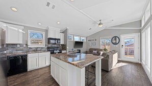 A spacious kitchen with white cabinets, a granite countertop, and a large island. There is a dining area with a couch and a TV. - The Resort at Fredericksburg Unit 29 (Fredericksburg)