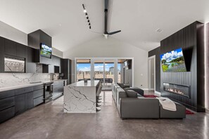A modern kitchen with a marble island, a dining area with a large table, a gray sofa, and a fireplace. - Freddy's Funkhouse - Fire Pit & On 290 Wine Trail (Fredericksburg)