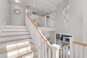 Eine Treppe mit Holzstufen und weißen Geländern, die zu einer Empfangshalle im zweiten Stock mit Kamin und Bücherregalen führt.