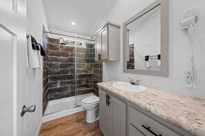 Een moderne badkamer met een douchewand van natuursteen, een wit wastafeltje en een wandhaardroger.