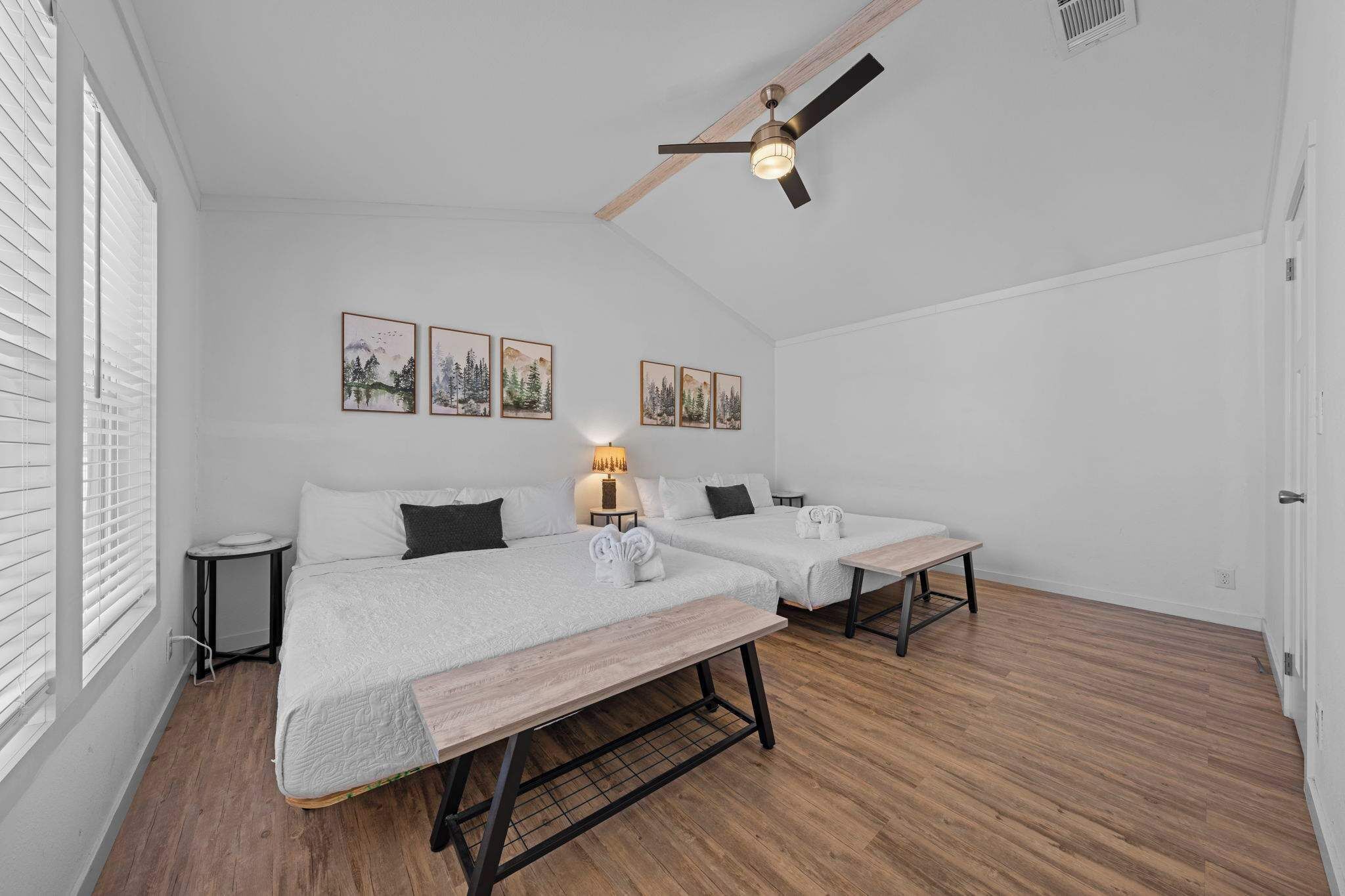 A room with two beds, a ceiling fan, and framed pictures on the wall.