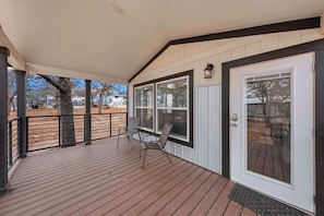 Eine überdachte Veranda mit Holzterrasse, zwei Stühlen und einer Tür mit Fensterteil.