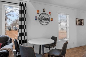 Ein Zimmer mit einem runden weißen Tisch, schwarzen Stühlen, einem schwarz-weiß karierten Vorhang und einer Wand mit einem Motorrad-Aufkleber.