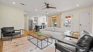 A modern living room with a sofa, two leather chairs, a coffee table, and a kitchen in the background.