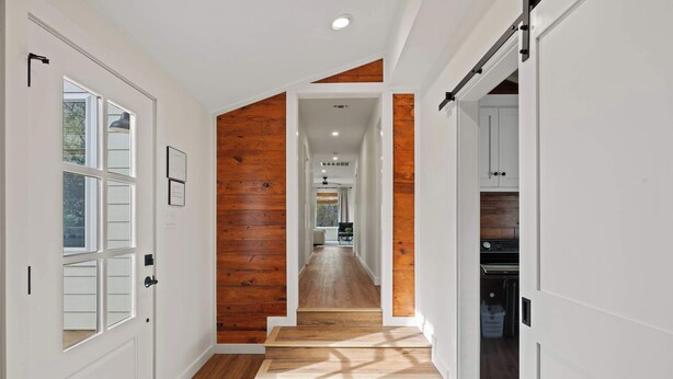 A hallway with wooden flooring and white walls, leading to a kitchen area with cabinets and appliances.