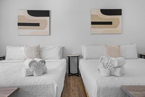Een hotelkamer met twee bedden, elk met witte beddengoed en opgerolde handdoeken. Aan de muren hangen abstracte schilderijen en er staat een klein tafeltje tussen de bedden.
