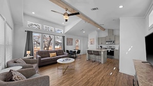 A spacious living area with a gray sofa, a coffee table, and a dining table with chairs. There is a kitchen area with a countertop and cabinets. - The Resort at Fredericksburg Unit 15 (Fredericksburg)