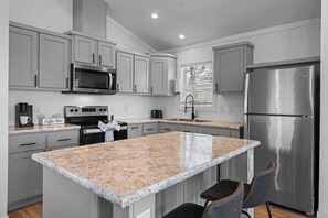 A modern kitchen with granite countertops, stainless steel appliances, and a central island with bar stools. - The Resort at Fredericksburg Unit 20 (Fredericksburg)